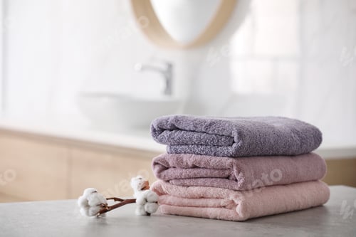 Preview: Stack of fresh towels and cotton flowers on table in bathroom