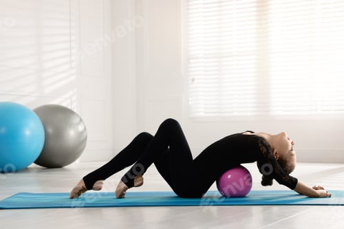 Preview: Cute little gymnast with ball stretching on mat indoors