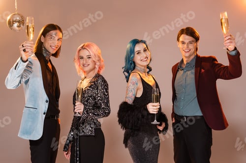 Preview: joyful nonbinary people in stylish clothes toasting with champagne and looking at camera on beige