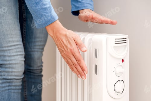 Preview: close up of Person Warming Hands Over Electric Radiator, Home Heating and Energy Efficiency concept