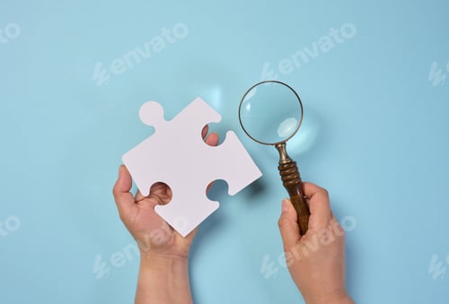 Preview: White empty puzzle and a magnifying glass in hand on a blue background