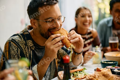 Preview: Young man enjoying in a taste of tacos while having lunch with friends in restaurant.