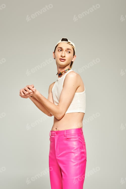 Preview: tattooed young gay man in baseball cap, crop top, bare belly and pink pants posing with clenched