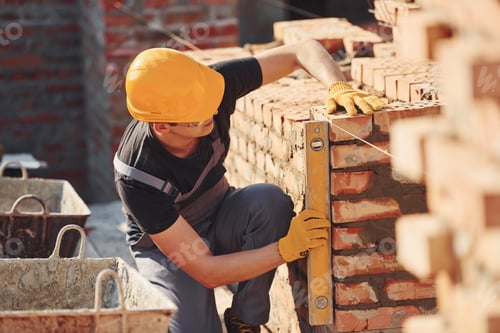 Preview: Measures of brick wall. Construction worker in uniform and safety equipment have job on building