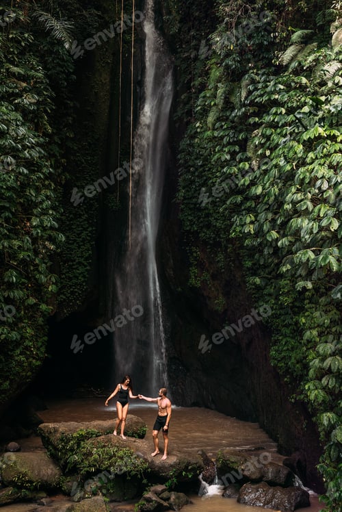 Preview: A man holds the hand of a beautiful woman at a waterfall. A couple in love on a waterfall