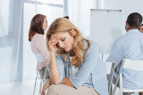Preview: upset mature woman looking down while multiethnic group sitting behind