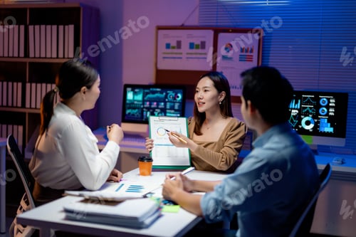 Preview: Asian business team analyzing financial data on clipboard and computer screen in office at night