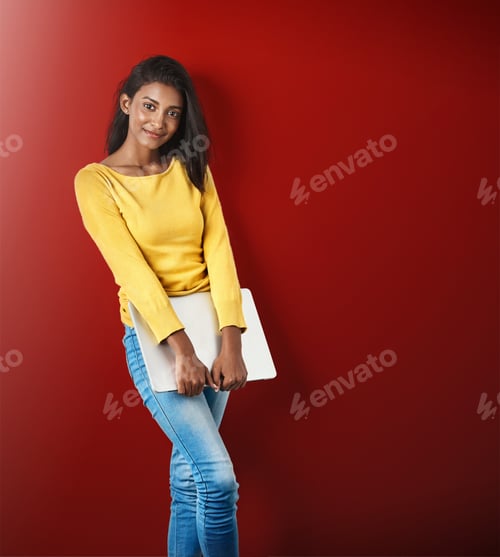 Preview: Studio portrait of an attractive young woman holding a laptop against a red background