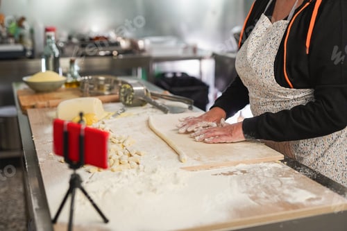 Preview: Italian senior woman doing home made gnocchi while using mobile phone for live stream