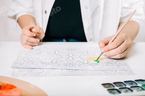Preview: Young woman coloring page antistress at table indoors, mental wellbeing and art therapy