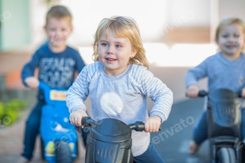 Preview: Girl and boys at preschool, racing push motorbikes in garden