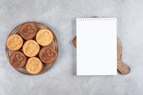 Preview: A notebook on a wooden board next to tart cookies on wooden board on marble background