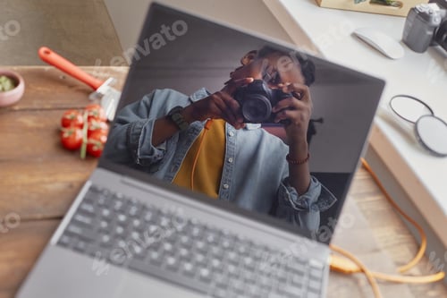 Preview: Young Adult Black Man Photographing Food Scene Reflected in Laptop Screen