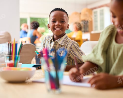 Preview: Grandchildren Indoors At Home Sitting At Table Drawing With Multi-Generation Family In Background