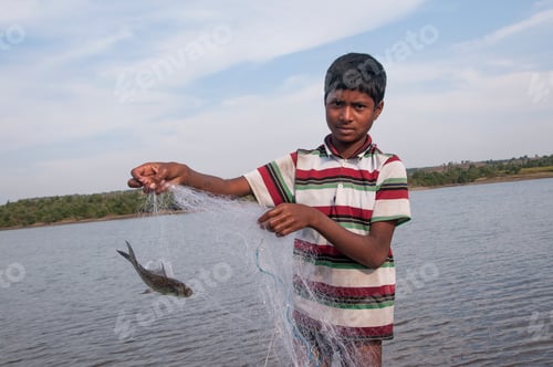 Preview: Young Fisherman take fish out of the net in front lake, India.