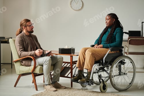 Preview: African American woman with disability sitting on wheelchair and talking to psychologist during
