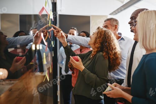 Preview: Laughing businesspeople brainstorming with sticky notes on a glass wall