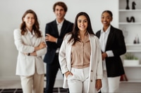 Preview: Latin businesswoman leader posing in office interior with her multiracial business team and smiling