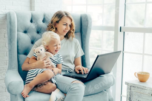 Preview: Mom and little daughter are sitting on an armchair with a laptop.