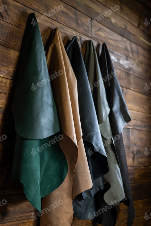Preview: Genuine leather of different colors for the production of clothes and shoes hangs on a wooden wall.