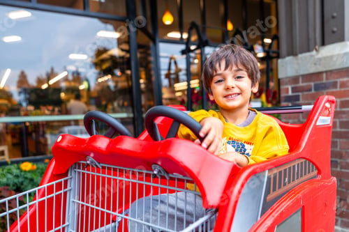 Preview: Happy child sitting in shopping cart outside supermarket