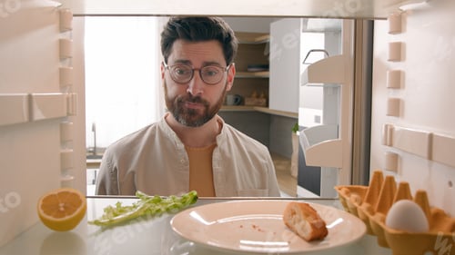 Preview: Hungry man guy open empty refrigerator with half lemon lettuce leaf one egg slice of bread leftover