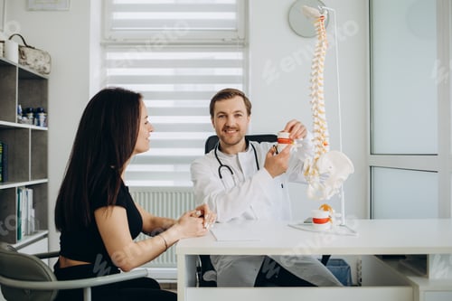 Preview: Male doctor showing to unrecognizable female patient problem with vertebra on special model sit