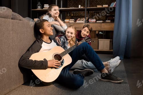 Preview: african american boy playing acustic guitar while his friends listening at home, teenagers playing