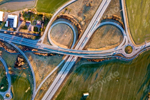 Preview: Aerial top view of modern highway road intersection, house roofs on spring green field background