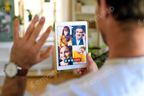 Preview: Rear view of unrecognizable man having video call on tablet at home