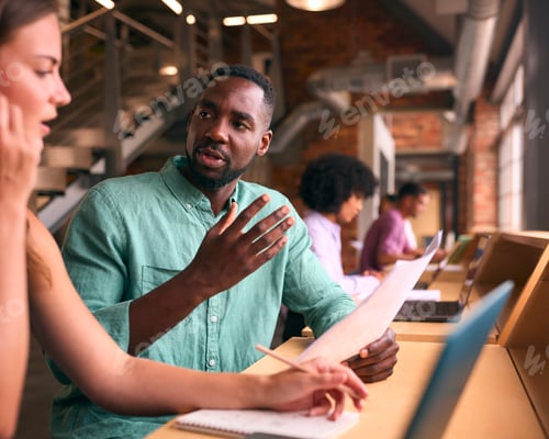 Preview: Male And Female Businesspeople Meeting In Office Discussing Documents With Colleagues In Background