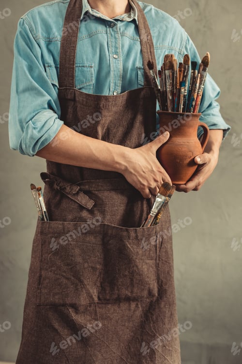 Preview: Man artist painter holding clay jug with paint brush. Painter artist and paintbrush in studio