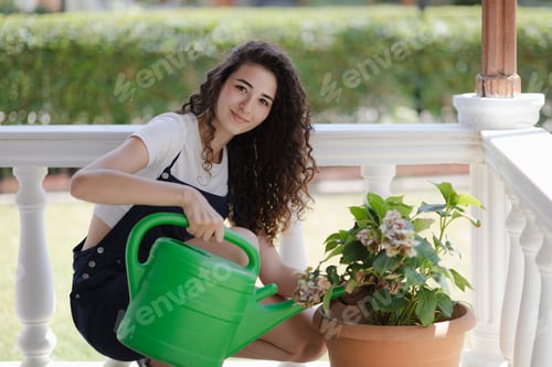 Preview: Young woman with curly hair working in the yard, watering flowers on terrace