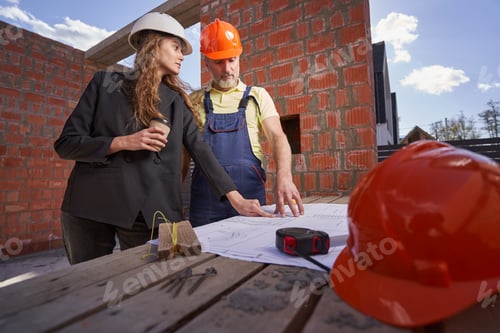 Preview: Female engineer pointing at blueprint to constructino worker