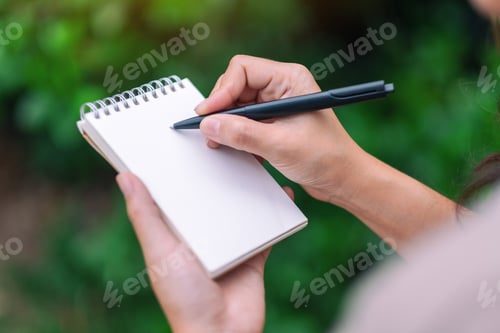 Preview: Closeup image of a woman holding and writing on blank notebook in the outdoors