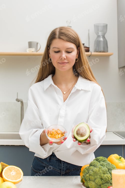 Visualização: A mulher segura abacate e cápsulas amarelas com vitamina D e ômega-3. Saúde e dieta.