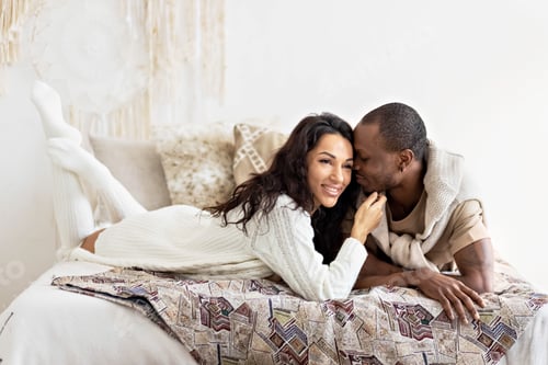 Preview: A couple in love - a black man and a mulatto woman on a bed in a bright room. Diverse family
