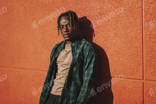 Preview: Handsome stylish Spanish man leaning on a red wall and posing with a serious face expression