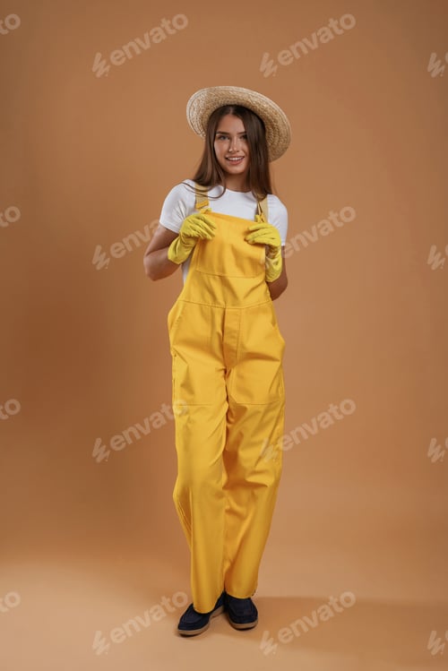 Preview: Garden worker is in straw hat. Young pretty woman is against background in the studio