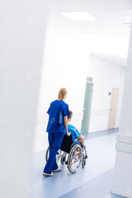 Preview: rear view of surgeon and upset patient in wheelchair in hospital corridor