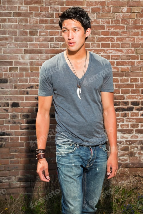 Preview: Urban Asian Man. Good Looking. Cool Guy. Wearing Grey Shirt And Jeans. Standing In Front Of Brick