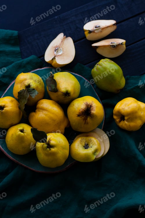 Preview: Yellow tart quince lies on a dark plate on a natural cloth on a black wooden background.