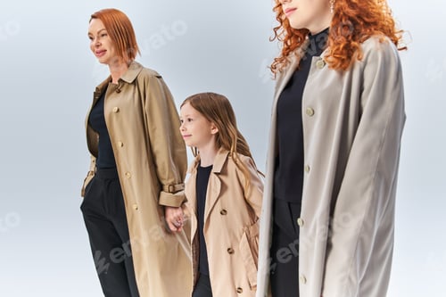 Preview: three generation redhead family walking together in stylish coats on grey backdrop, autumn fashion