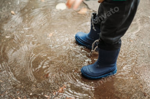 Preview: Boy feet in rubber boots while playing outside on a rainy day