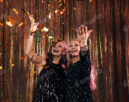 Preview: Two smiling senior women in black dresses throwing colorful confetti