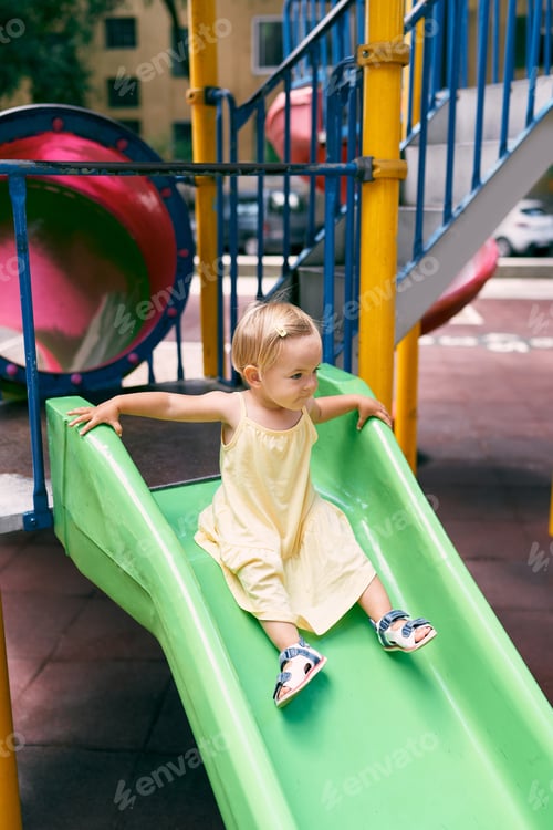 Preview: Little girl in a dress slides down a slide on the playground