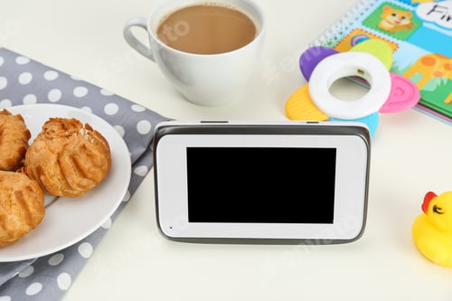 Preview: Modern monitor, cup of coffee, cookies and baby accessories on table, space for text. CCTV equipment