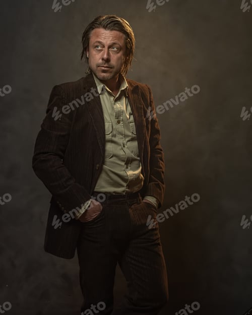 Preview: Fashionable Middle Aged Man In Dark Brown Suit In Front Of Grey Wall. Low Key Studio Shot.