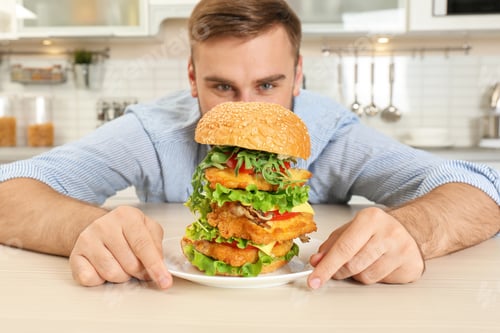 Preview: Young hungry man and huge burger in kitchen