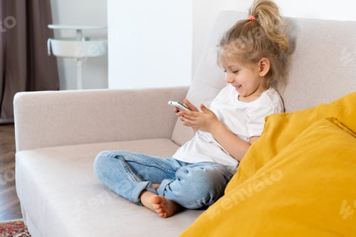 Preview: a little blonde girl at home on the sofa with a mobile phone, children and gadgets